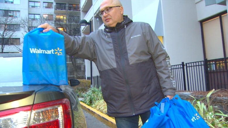 Un hombre recibe su entrega semanal de comestibles de Walmart.  Sus productos están empacados en ocho bolsas reutilizables. 