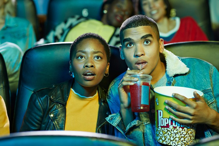 Pareja viendo una película en un teatro lleno de gente mientras disfruta de palomitas de maíz y bebidas.